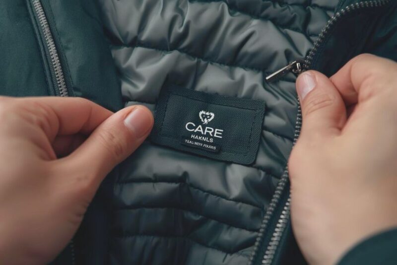 Close-up of hands holding open a jacket care label, zippers visible.